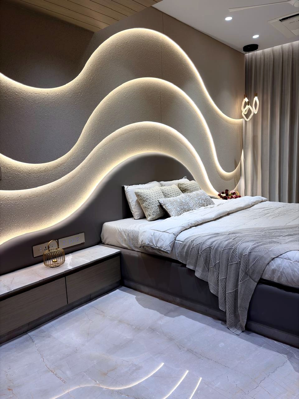 The master bedroom — a stepped, wave-lit curved wall in textured plaster rising behind a low grey bed