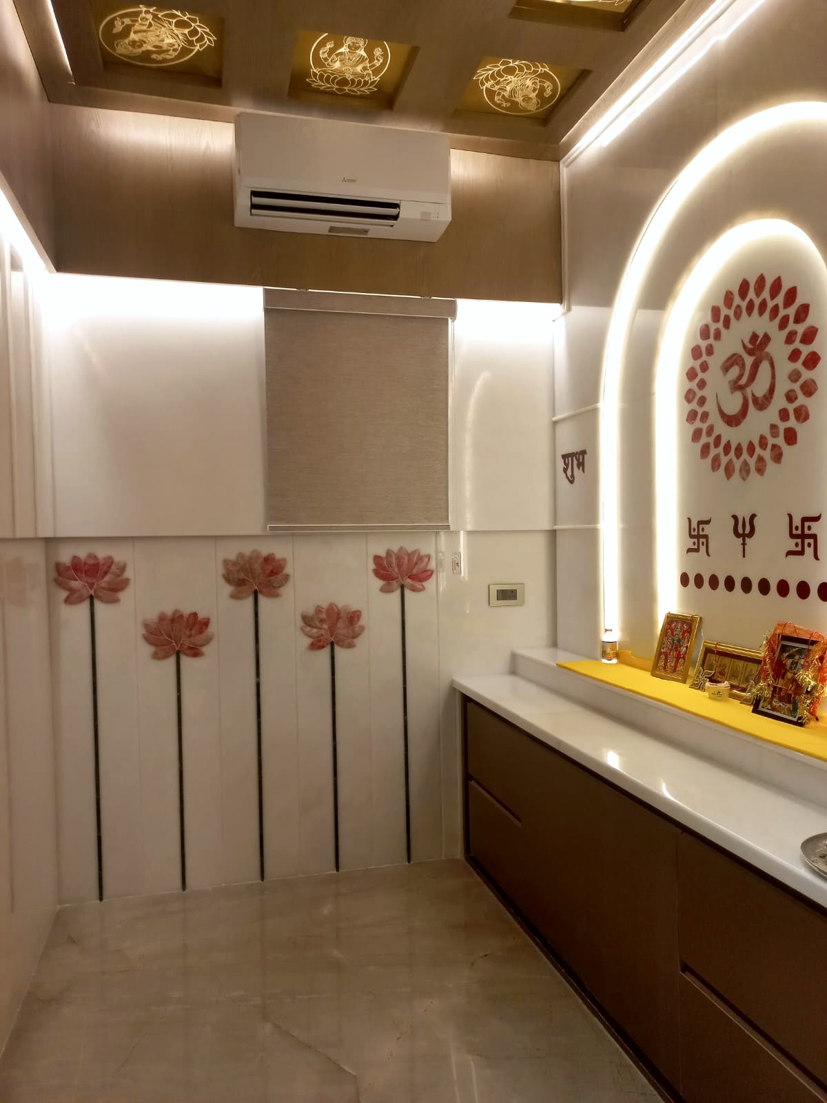 The mandir interior — backlit arch with Om and a lotus medallion, a row of pink lotus motifs on the white dado, deities on a marble ledge, gold-leaf lotus ceiling panels