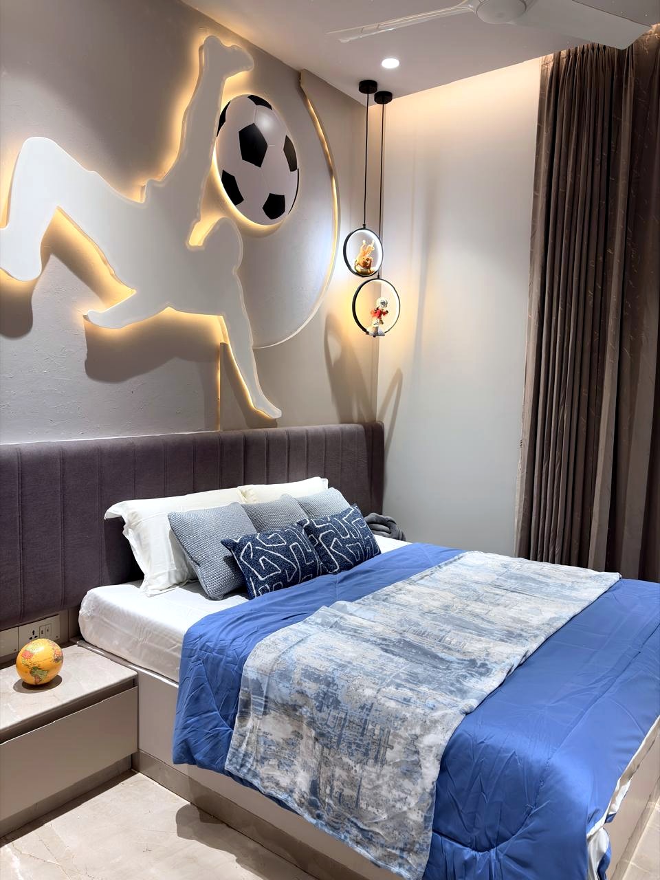 The son's bedroom — a backlit footballer silhouette with a football, a grey channel-tufted bed, blue bedding, dual ring pendant lights