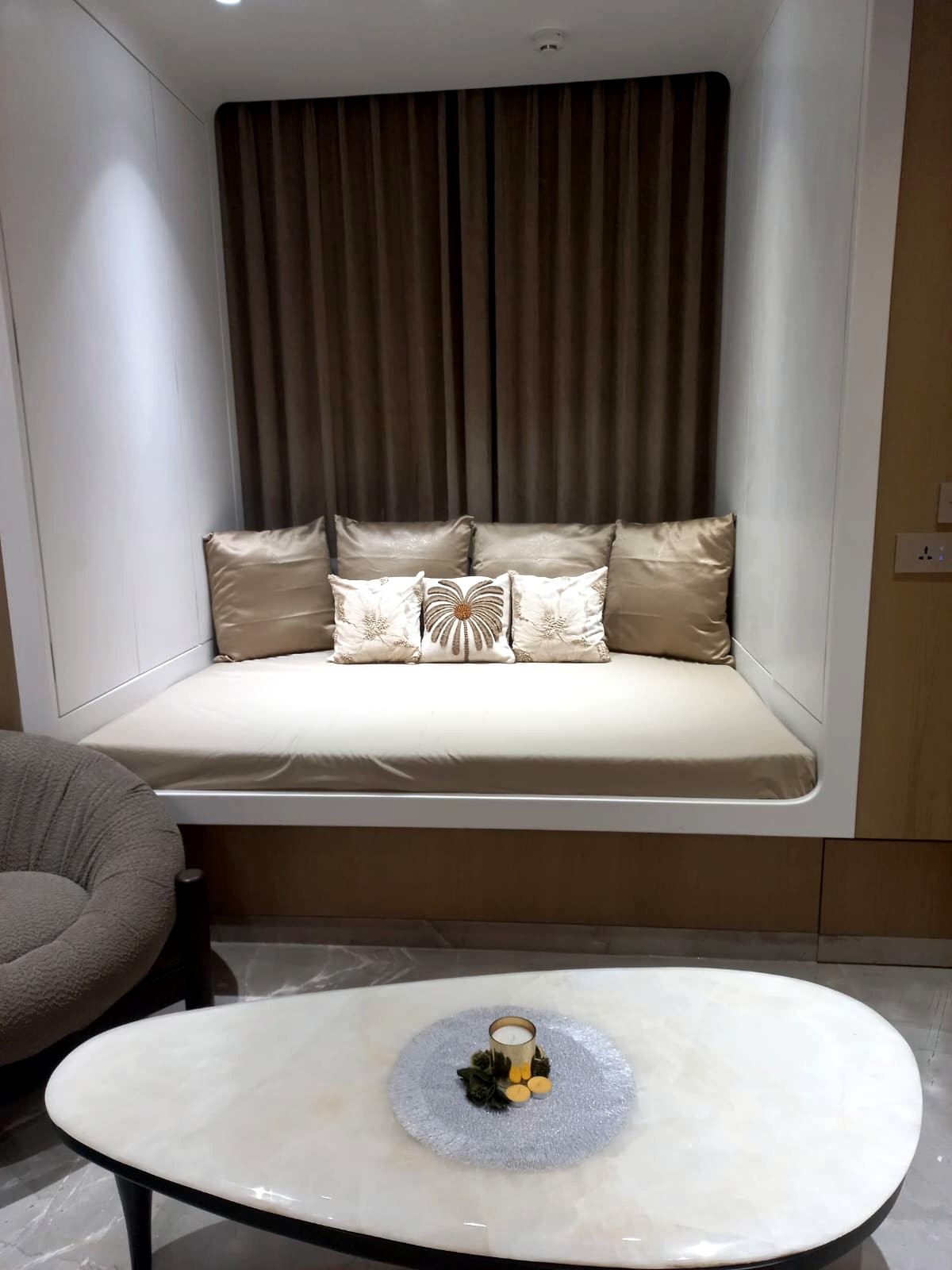 The family room daybed — a curved white niche holding a cushioned daybed against a brown curtain, with the marble coffee table in the foreground