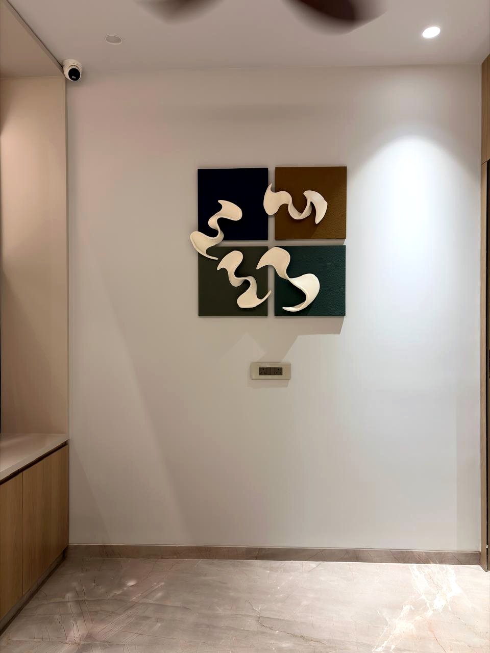 A wall near the entrance — four square relief panels in navy, ochre, and forest green with pale sculptural forms set across them