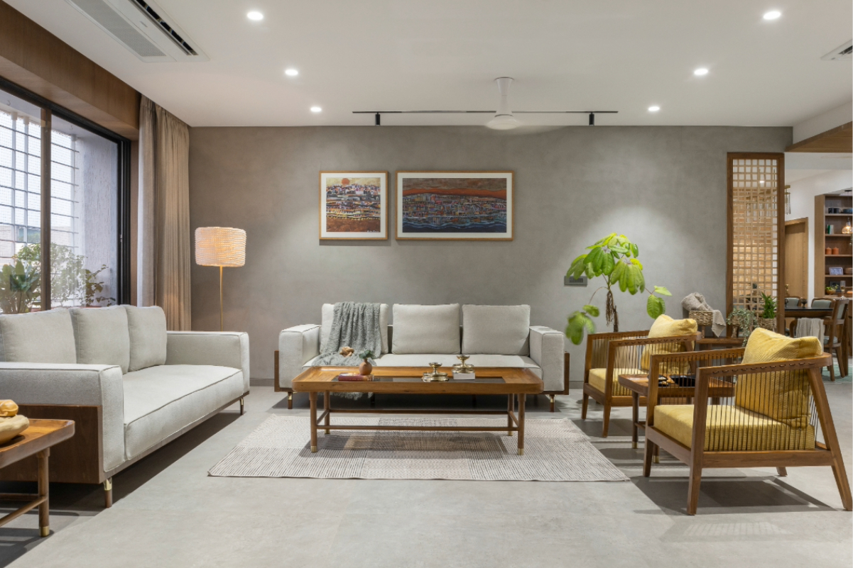 The living room — grey sofas, teak coffee table, two framed paintings on the grey plaster wall, lattice screen to the dining beyond