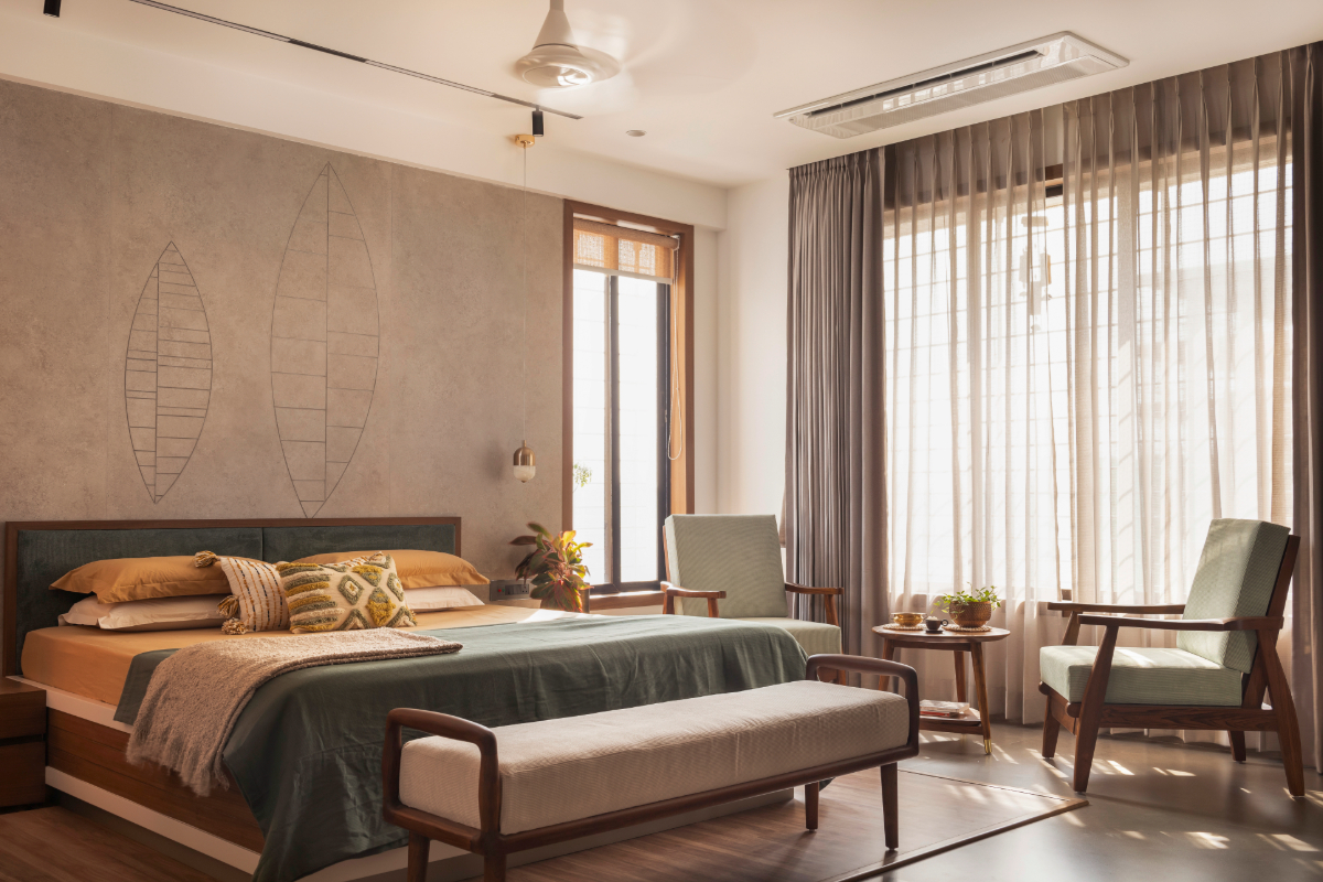 The master bedroom — green bedding, dark headboard on raised timber platform, grey plaster wall with incised leaf motifs, mint armchairs at the window