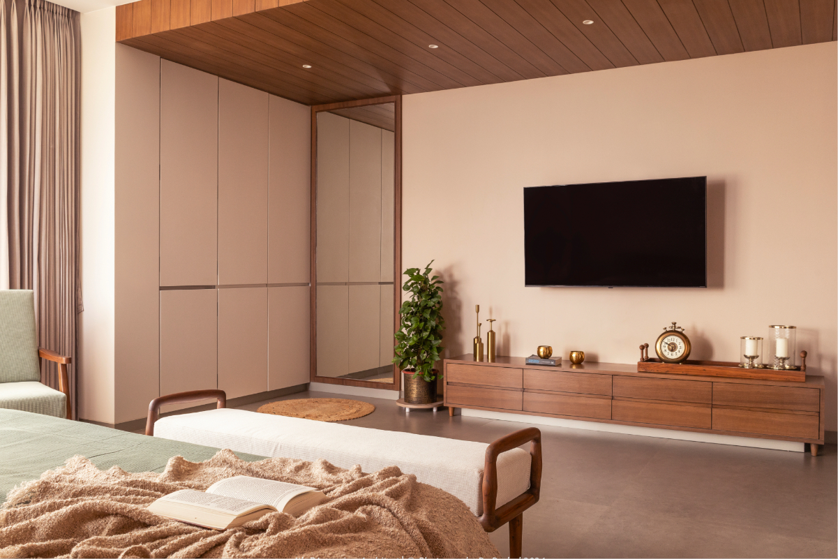 The master bedroom TV wall — taupe cabinetry with a mirror panel, teak TV unit with brass accessories, the bed and platform in the foreground