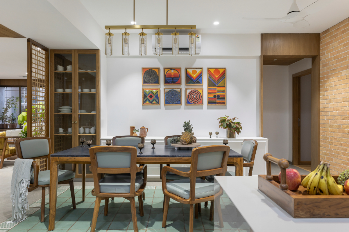 Wide view of the dining room — grid of eight framed paintings, green tile wall, dining table, brass pendant