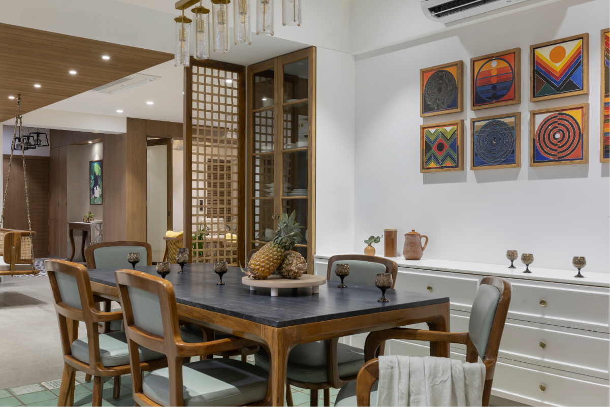 View into the dining room through the timber lattice screen — table, paintings, brick wall, the jhula and living room visible in the background