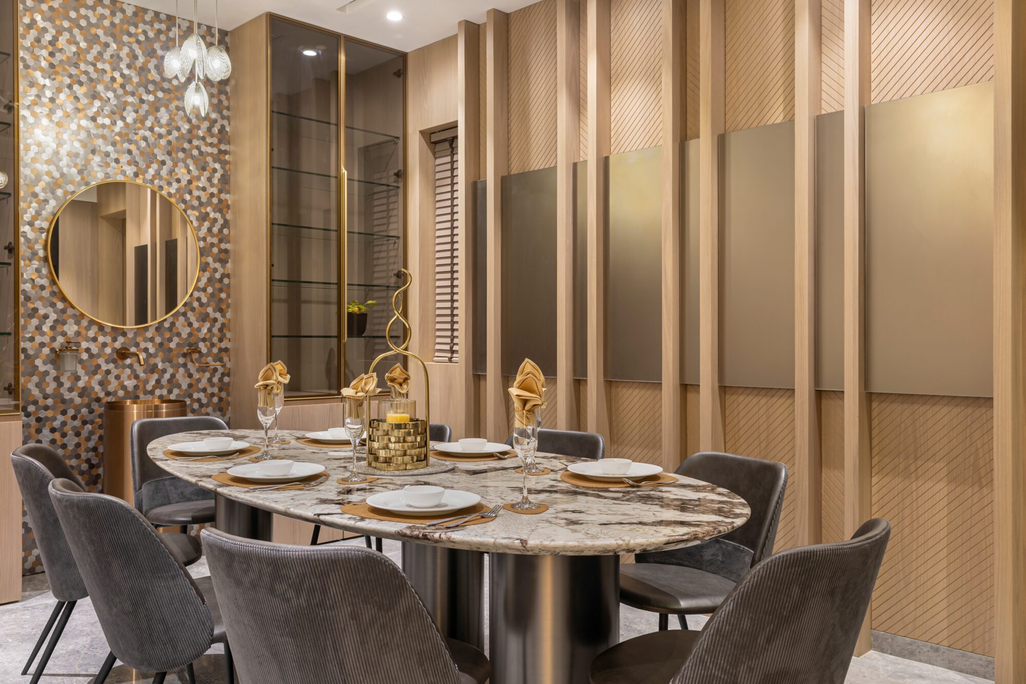 The dining room — oval marble-topped table, grey velvet chairs, mosaic feature wall with circular mirror, fluted oak panelling
