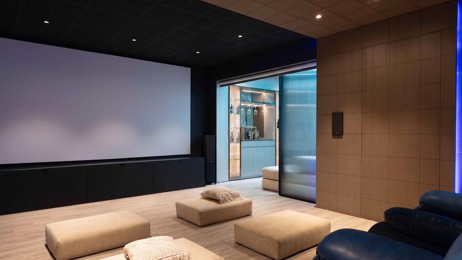 Wide view of the home theatre with the projector screen on the left and the glass-walled bar visible through sliding doors on the right