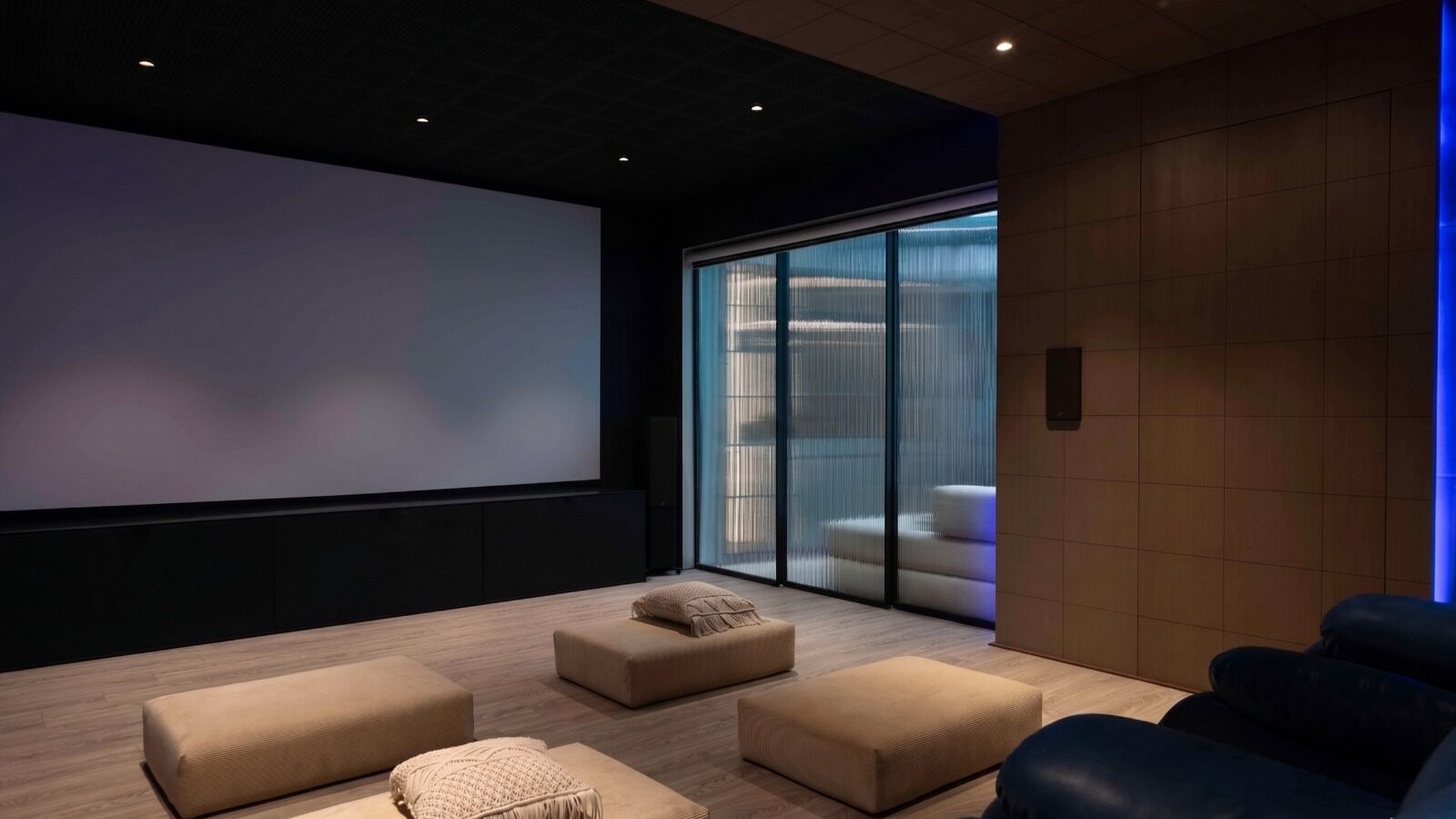 The same home theatre at night, screen on, sliding doors closed, blue mood lighting through the fluted glass