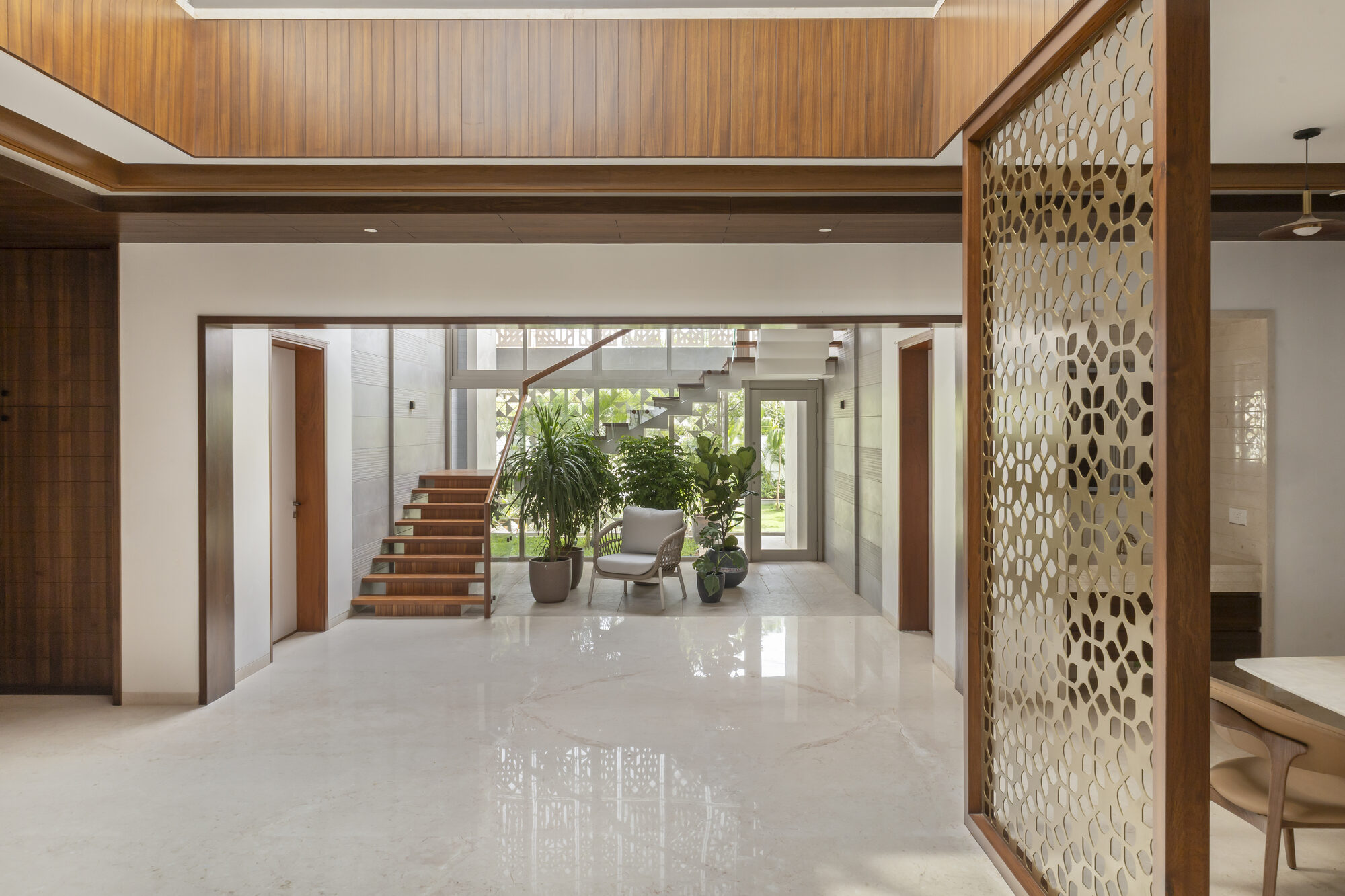 Entrance foyer with double-height timber ceiling, brass jali screen, and view to the staircase