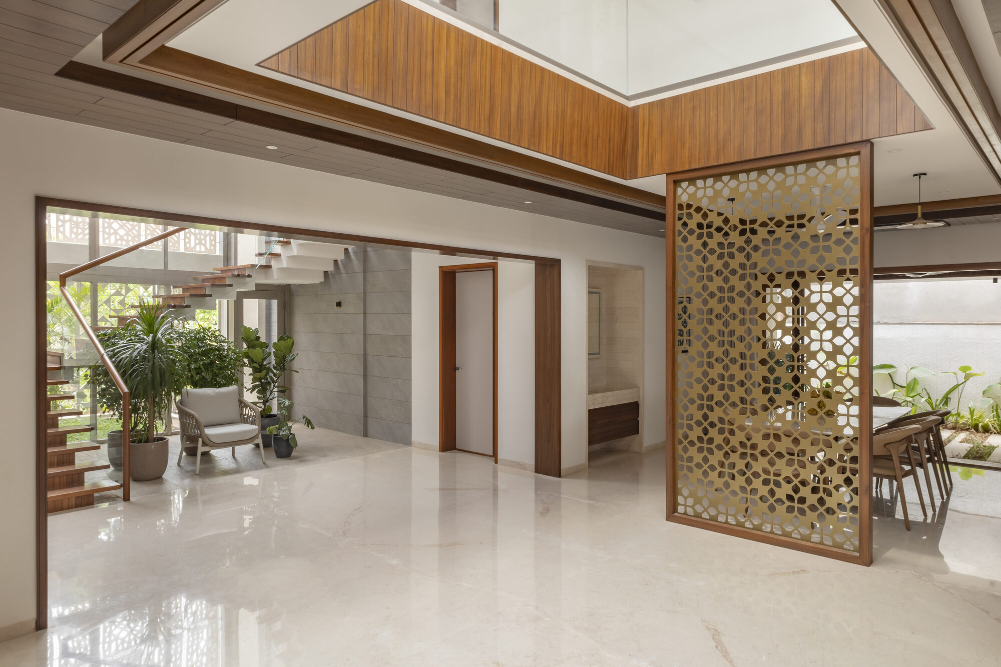 Wide view of the foyer with the double-height timber ceiling, brass jali screen on the right, and staircase beyond